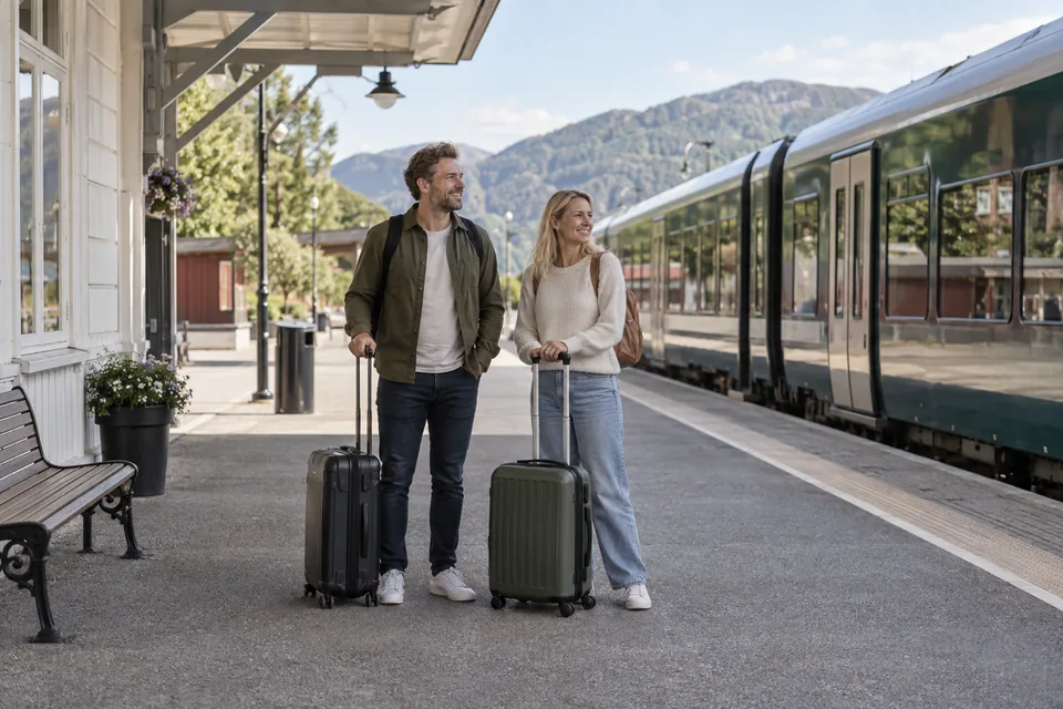KI-generert illustrasjon: Et par med små kofferter venter ved en togstasjon.