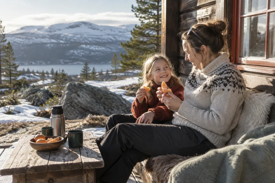 KI-generert illustrasjon: En voksen og et barn sitter på en hyttebenk i vårsolen med appelsiner og en termos.