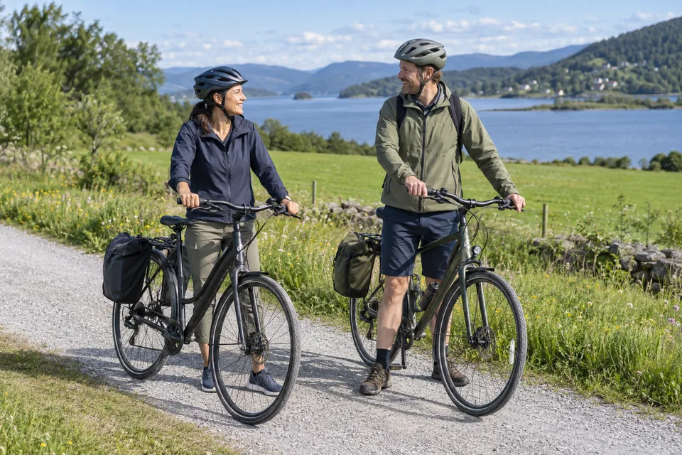 KI-generert illustrasjon: To voksne med sykkelhjelm tar en pause ved syklene på en bred grussti.
