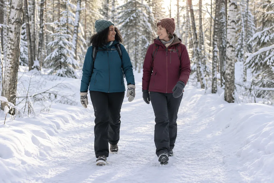 KI-generert illustrasjon: To venninner går sammen på en bred snødekt skogssti.